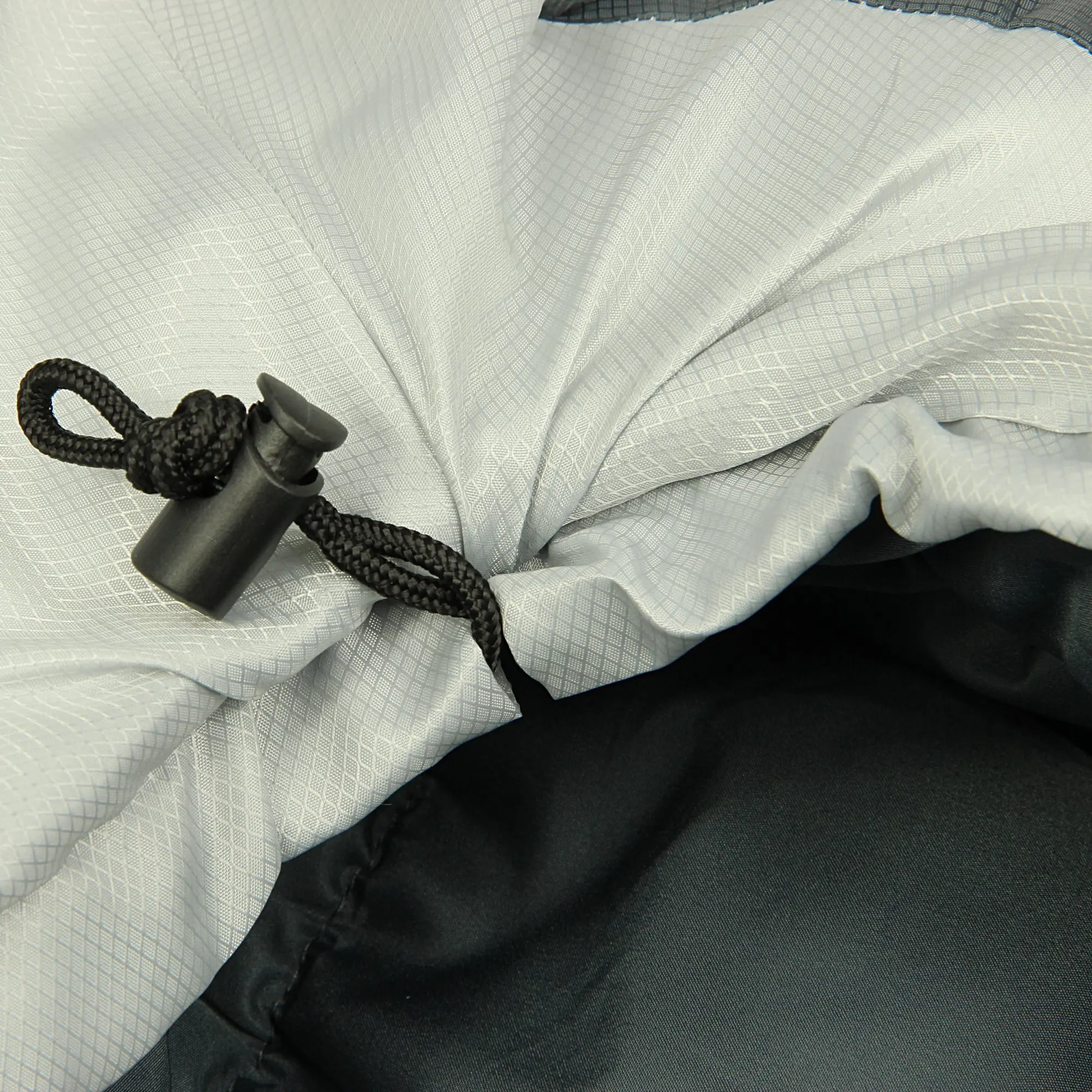 Nahaufnahme eines grauen, gewebten Stoffes mit einem schwarzen Kordelzug und einem Kordelstopper, der die Öffnung eines dunkleren, glatten Stoffbereichs zusammenzieht.