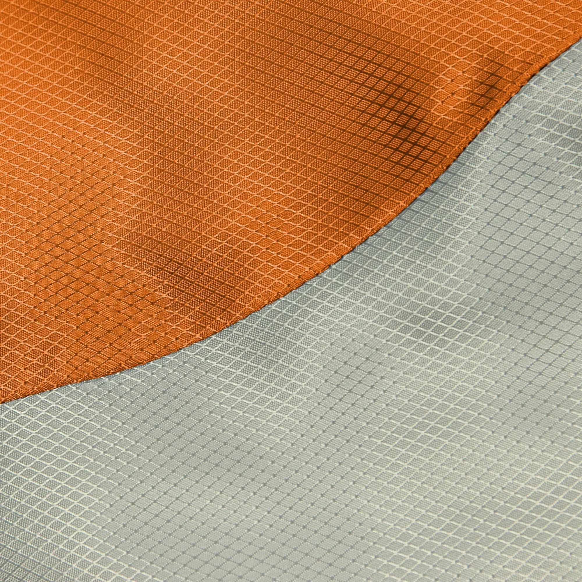 Ein Detailbild von einem Textilstück mit orangefarbenem und grauem Stoff, die durch eine Kurvenlinie getrennt sind, wobei beide Stoffe ein gitterartiges Strukturmuster aufweisen.