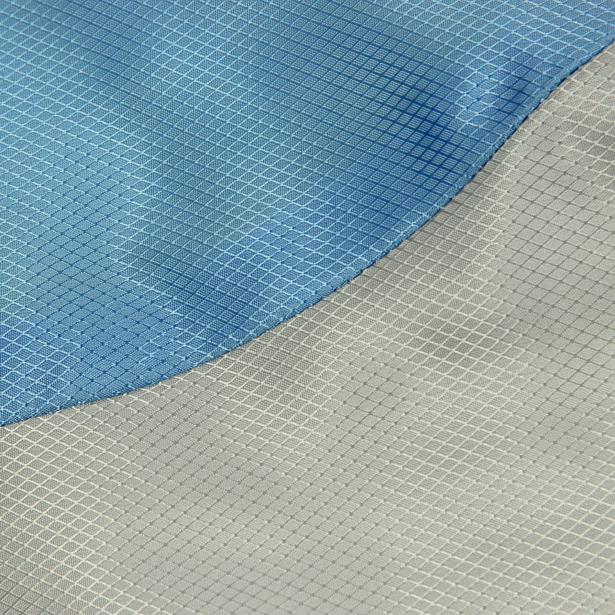Nahaufnahme eines Stoffes mit diagonalen Linienmustern in Blau und Grau, die durch eine geschwungene Naht getrennt sind, zeigt eine strukturierte, rautenförmige Gewebestruktur.