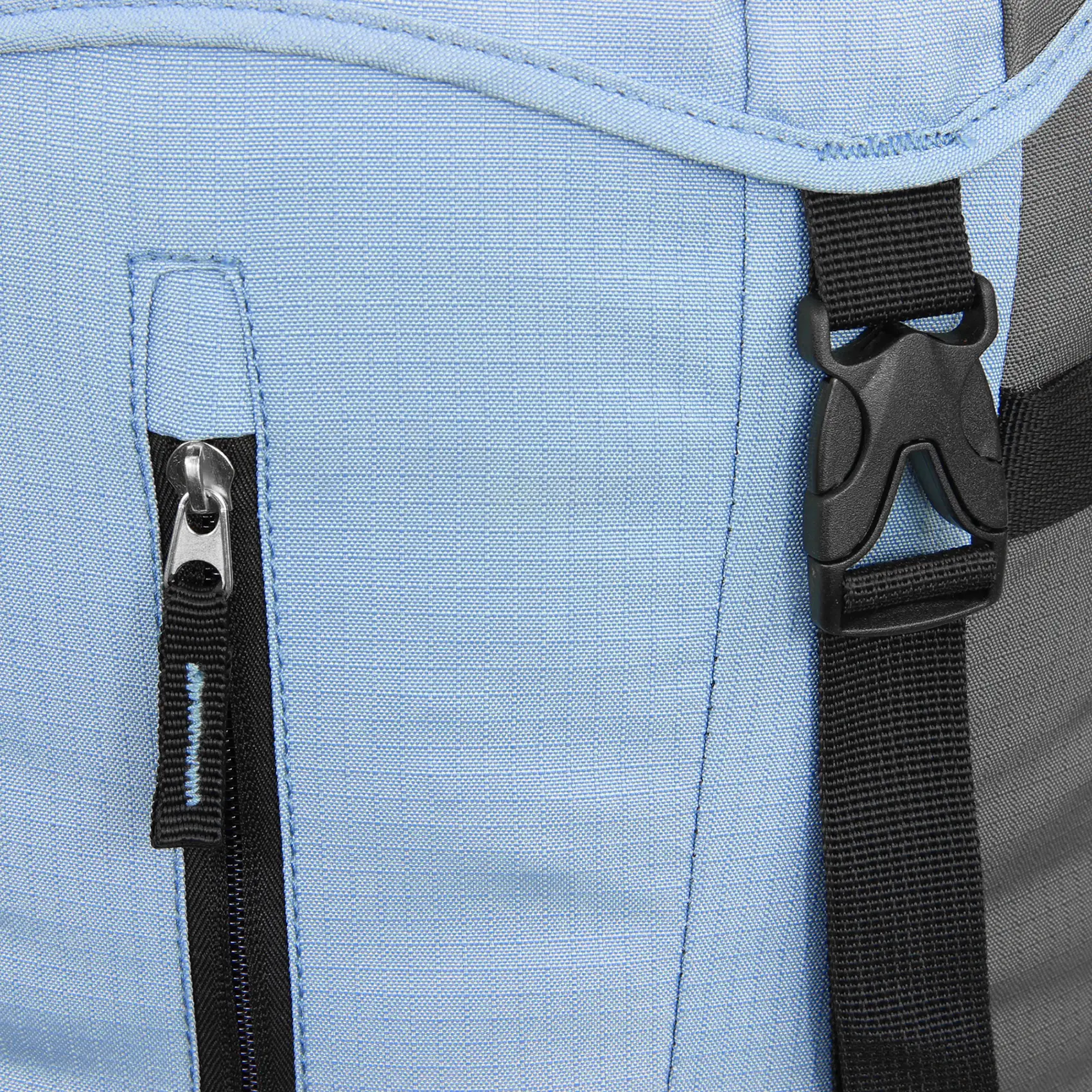 A close-up of a light blue backpack showing a zipper pocket and a black plastic buckle attached to a black strap.