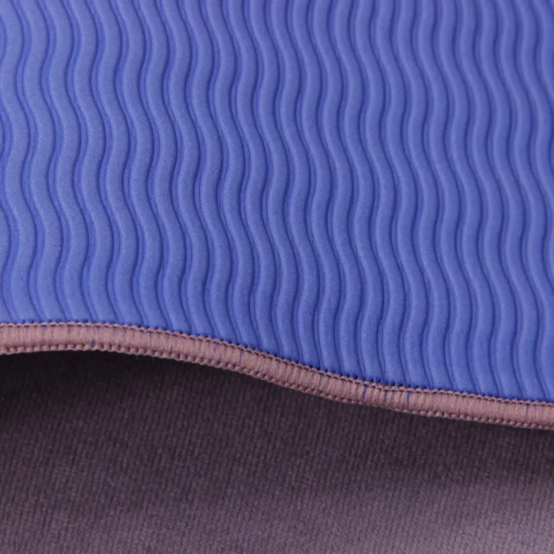 Nahaufnahme eines blauen Stoffstücks mit wellenförmigem Muster und einer rosa Ziernaht am Rand, darüber befindet sich ein brauner Stoff.